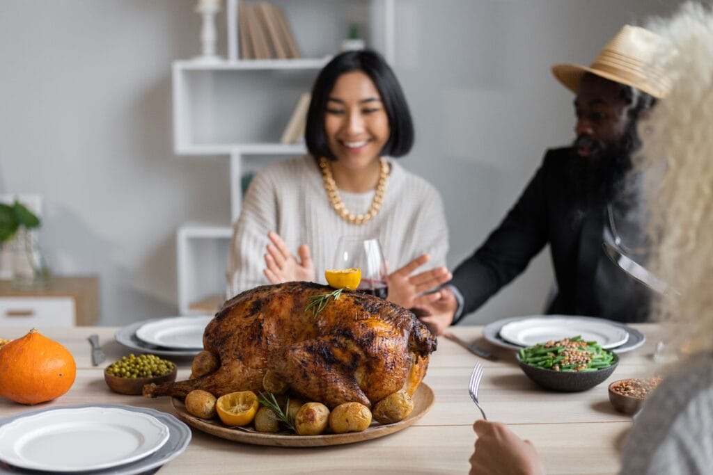 Cheerful multiethnic people having dinner together at table with roasted turkey while celebrating Thanksgiving Day