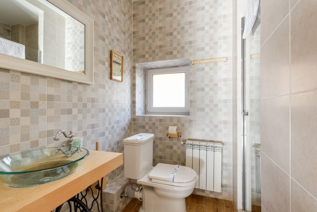 Bright bathroom featuring a contemporary glass sink, modern tiles, and natural light through the window. With a running toilet